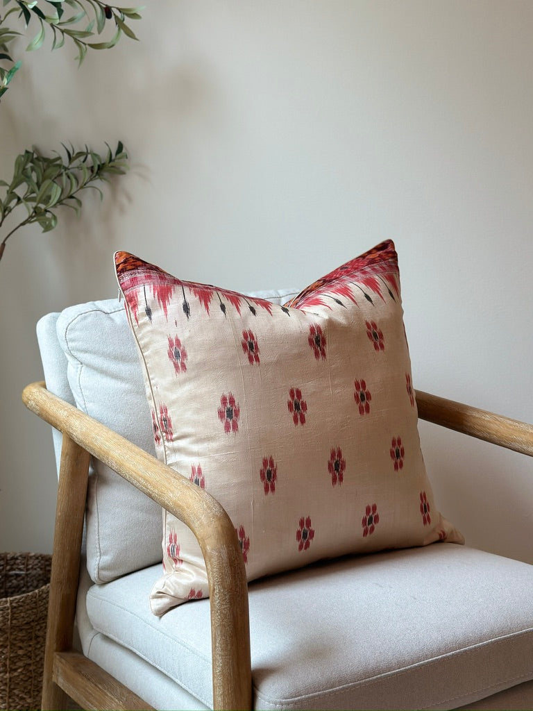 A handcrafted 20x20 pillow cover made from vintage silk sari fabric, featuring a cream background with red and black ikat-inspired floral patterns. The cushion is bordered with a subtle red and black design, showcasing intricate silk weaving techniques.