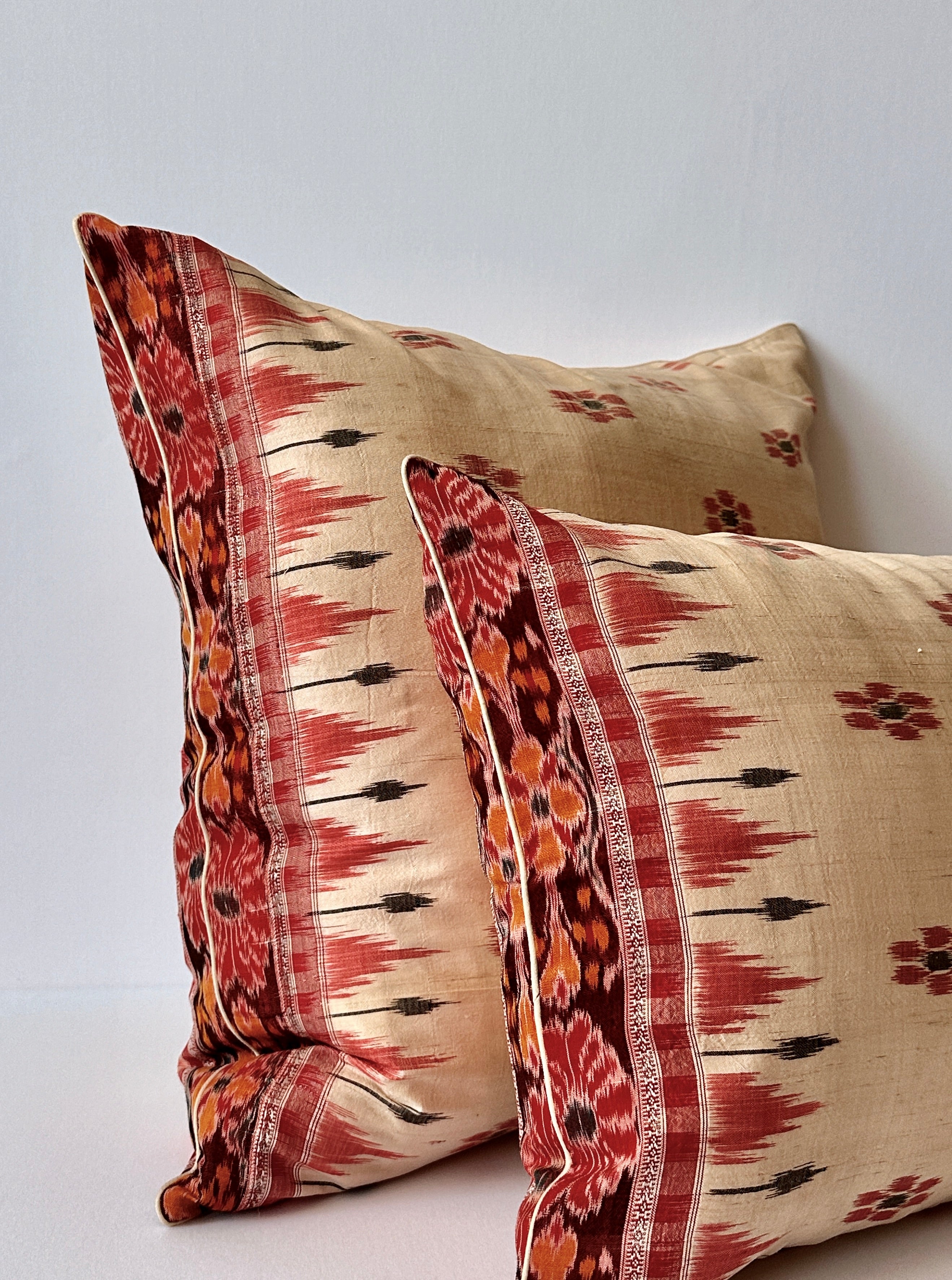 A handcrafted 20x20 pillow cover made from vintage silk sari fabric, featuring a cream background with red and black ikat-inspired floral patterns. The cushion is bordered with a subtle red and black design, showcasing intricate silk weaving techniques.