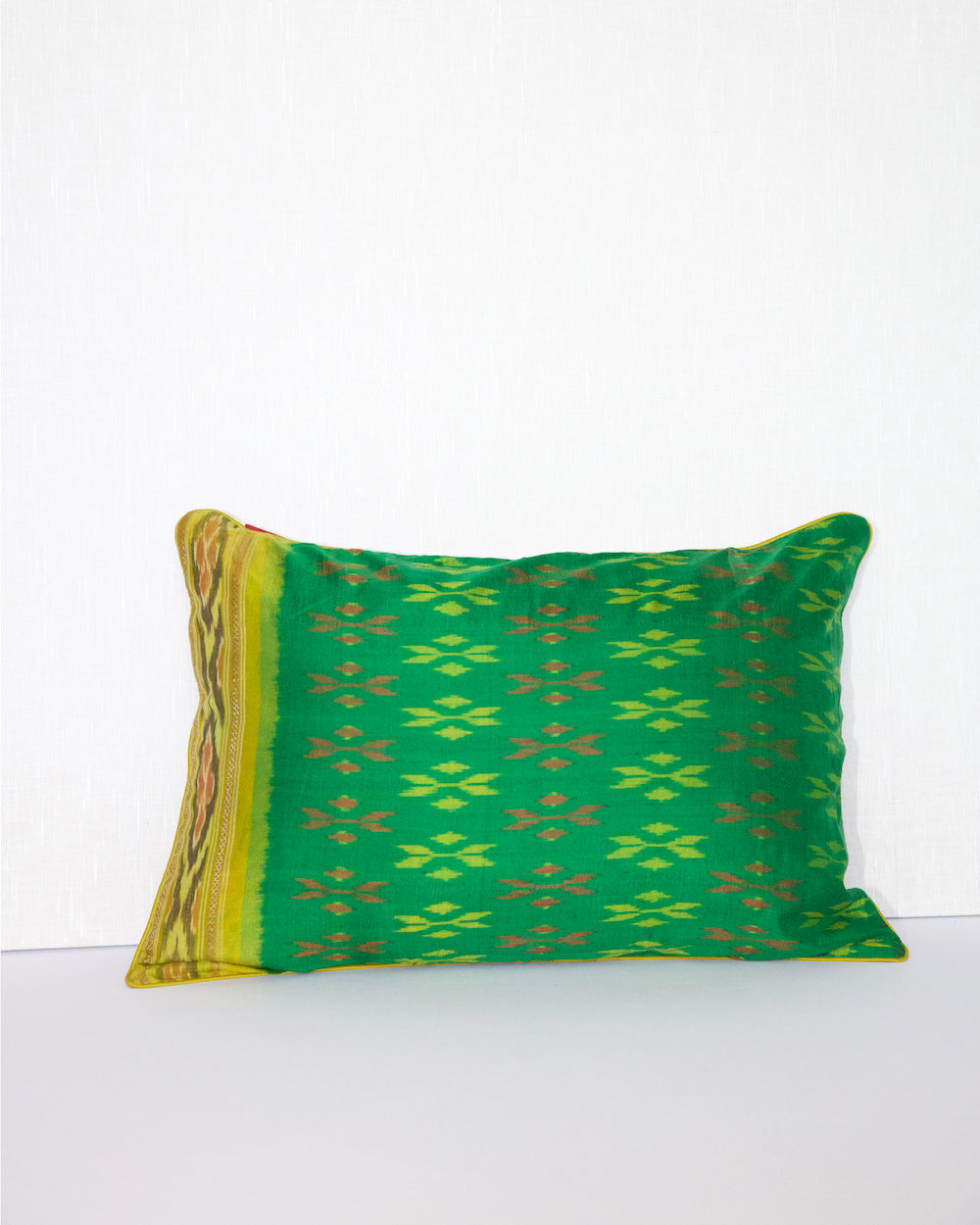 A handcrafted 20x20 pillow cover made from vibrant green silk with traditional ikat-inspired patterns in yellow and rust. The cushion’s border features an intricate design, adding a touch of artisanal craftsmanship and cultural flair to any decor