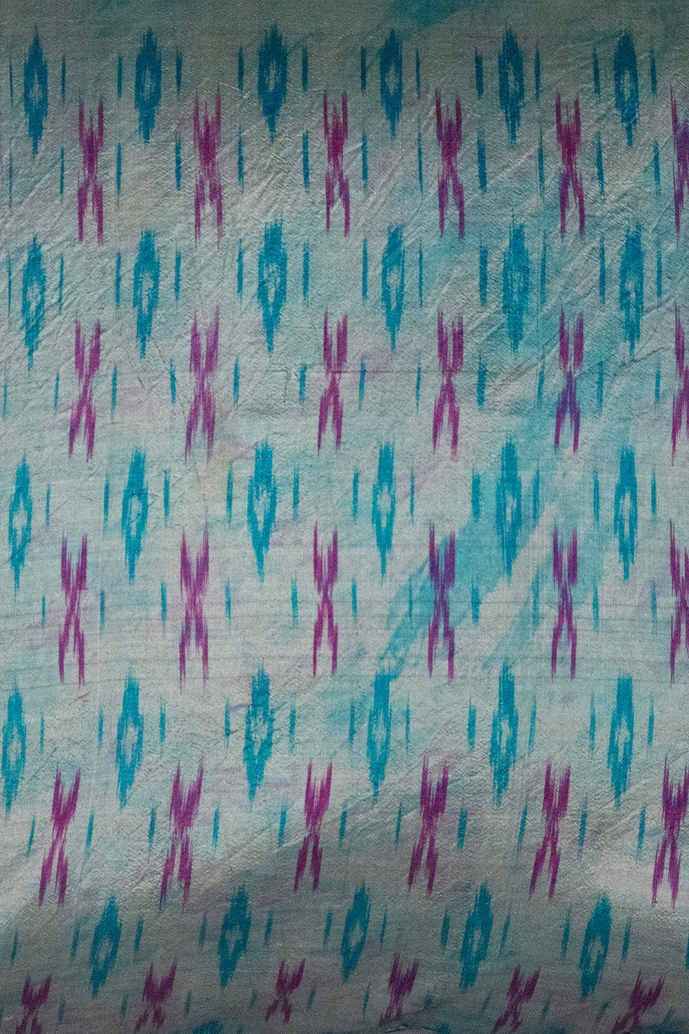 A handcrafted 20x20 pillow cover made from vintage silk fabric, featuring a vibrant ikat pattern in shades of blue and pink. The cushion showcases a unique blend of traditional weaving techniques with a modern, bold color palette.