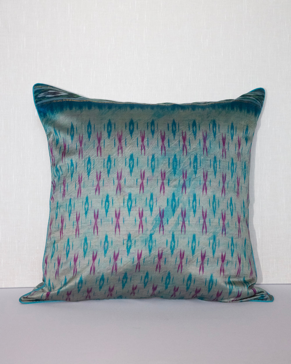 A handcrafted 20x20 pillow cover made from vintage silk fabric, featuring a vibrant ikat pattern in shades of blue and pink. The cushion showcases a unique blend of traditional weaving techniques with a modern, bold color palette.