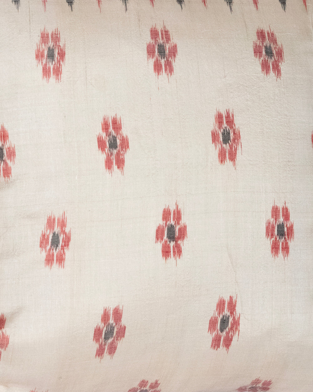 A handcrafted 20x20 pillow cover made from vintage silk sari fabric, featuring a cream background with red and black ikat-inspired floral patterns. The cushion is bordered with a subtle red and black design, showcasing intricate silk weaving techniques.