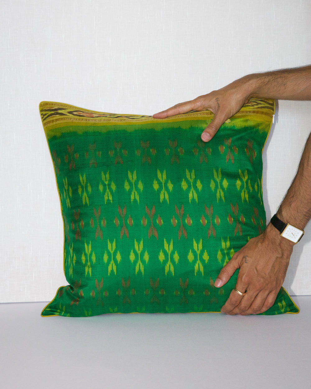 A handcrafted 20x20 pillow cover made from vibrant green silk with traditional ikat-inspired patterns in yellow and rust. The cushion’s border features an intricate design, adding a touch of artisanal craftsmanship and cultural flair to any decor