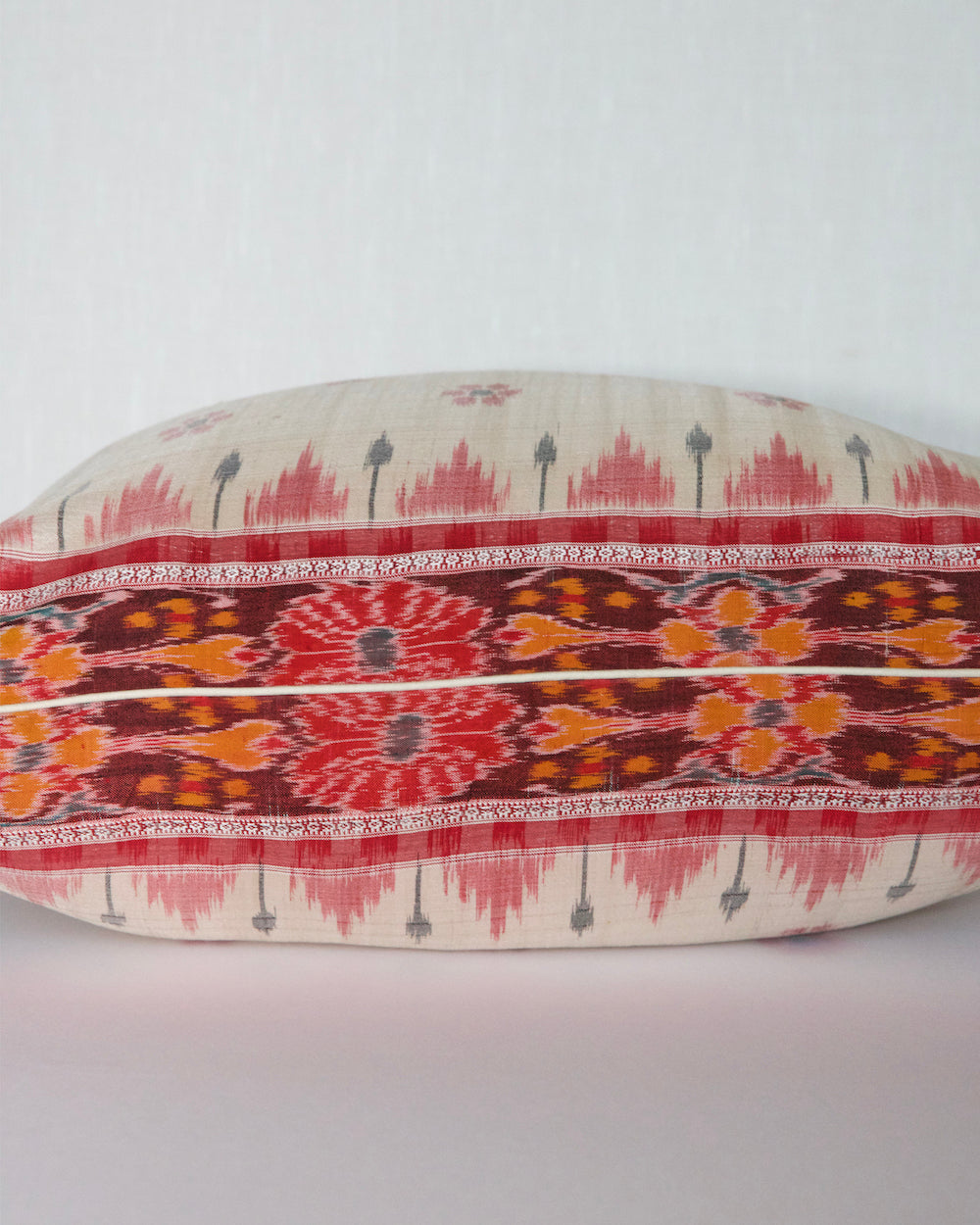 A handcrafted 20x20 pillow cover made from vintage silk sari fabric, featuring a cream background with red and black ikat-inspired floral patterns. The cushion is bordered with a subtle red and black design, showcasing intricate silk weaving techniques.