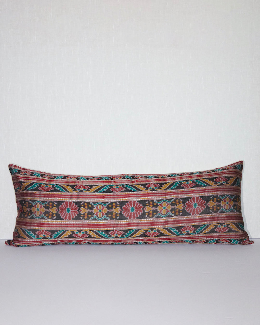A unique lumbar pillow featuring intricate geometric and floral motifs in warm tones of red, teal, yellow, and beige, set against a black background. The handcrafted design offers a rich, bohemian aesthetic with vintage textile craftsmanship.