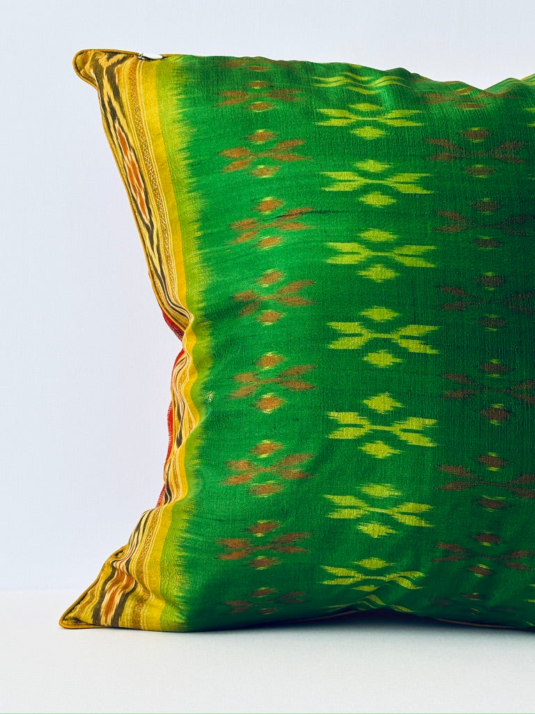 A handcrafted 20x20 pillow cover made from vibrant green silk with traditional ikat-inspired patterns in yellow and rust. The cushion’s border features an intricate design, adding a touch of artisanal craftsmanship and cultural flair to any decor