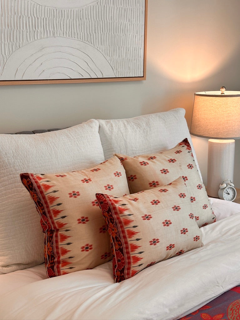 A handcrafted 20x20 pillow cover made from vintage silk sari fabric, featuring a cream background with red and black Ikat floral patterns. The cushion is bordered with a subtle red and black design, showcasing intricate silk weaving techniques.