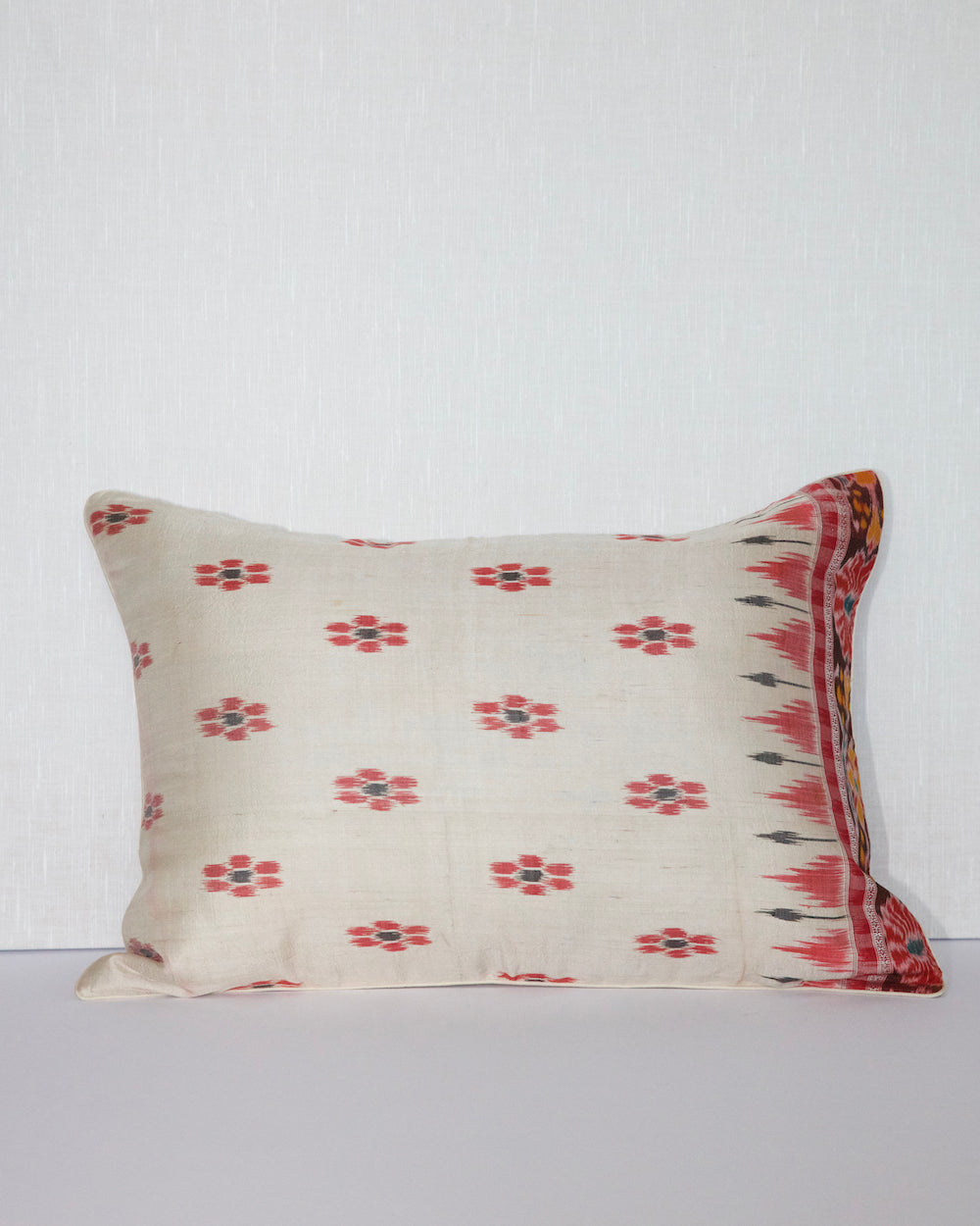 A handcrafted 20x20 pillow cover made from vintage silk sari fabric, featuring a cream background with red and black ikat-inspired floral patterns. The cushion is bordered with a subtle red and black design, showcasing intricate silk weaving techniques.