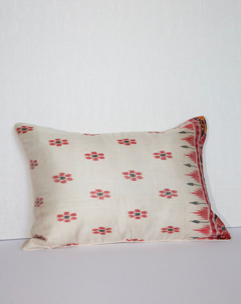 A handcrafted 20x20 pillow cover made from vintage silk sari fabric, featuring a cream background with red and black ikat-inspired floral patterns. The cushion is bordered with a subtle red and black design, showcasing intricate silk weaving techniques.