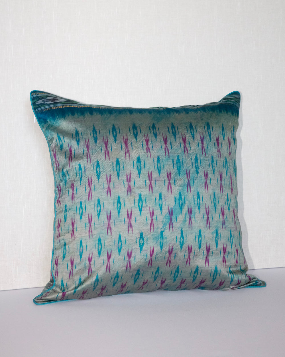 A handcrafted 20x20 pillow cover made from vintage silk fabric, featuring a vibrant ikat pattern in shades of blue and pink. The cushion showcases a unique blend of traditional weaving techniques with a modern, bold color palette.