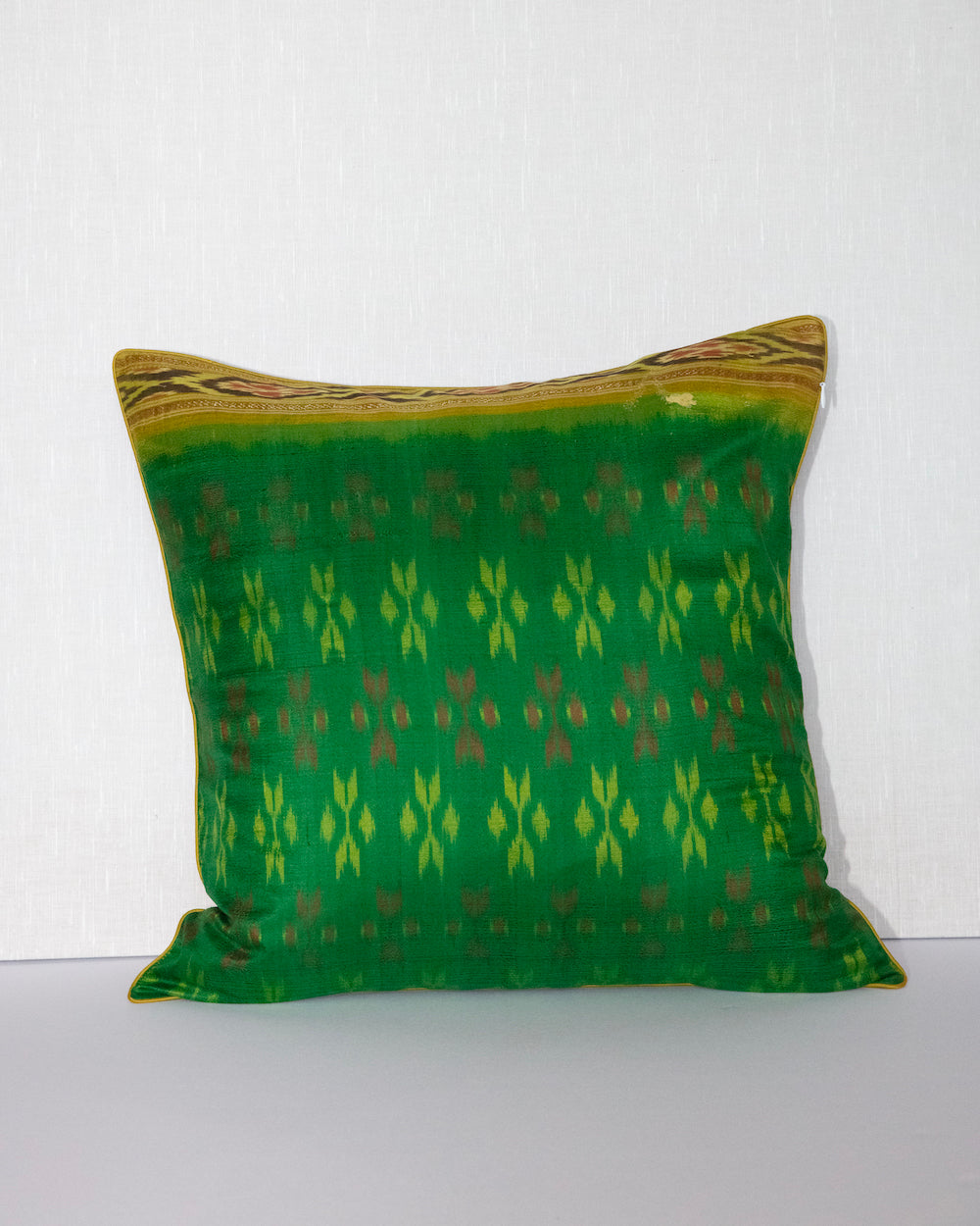 A handcrafted 20x20 pillow cover made from vibrant green silk with traditional ikat-inspired patterns in yellow and rust. The cushion’s border features an intricate design, adding a touch of artisanal craftsmanship and cultural flair to any decor